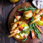 Overhead shot of two glasses filled with autumn harvest white sangria, garnished with rosemary and cinnamon sticks.