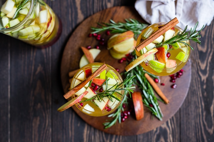 Overhead shot of two glasses filled with autumn harvest white sangria, garnished with rosemary and cinnamon sticks.