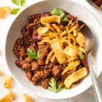 Bowl of beef and bean chili with cheese and corn chips.