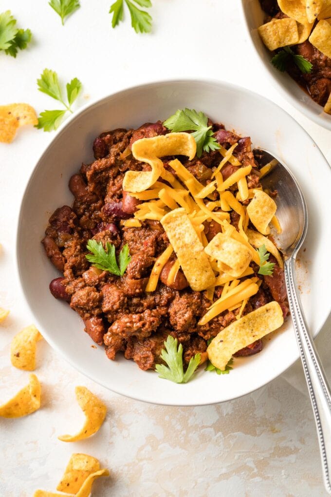 Bowl of beef and bean chili with cheese and corn chips.
