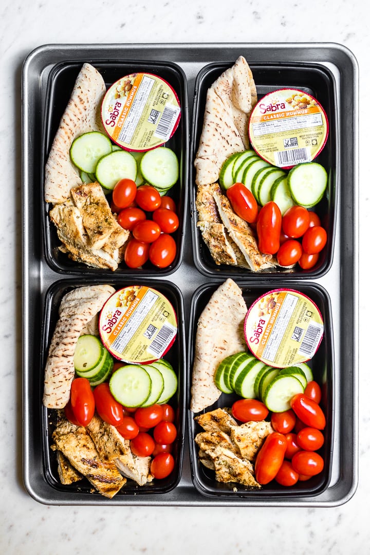 Four prepped chicken hummus bistro boxes arranged on a sheet pan.