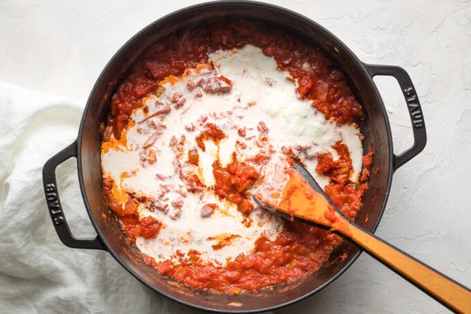 Cream just poured into a pan of tomato sauce.