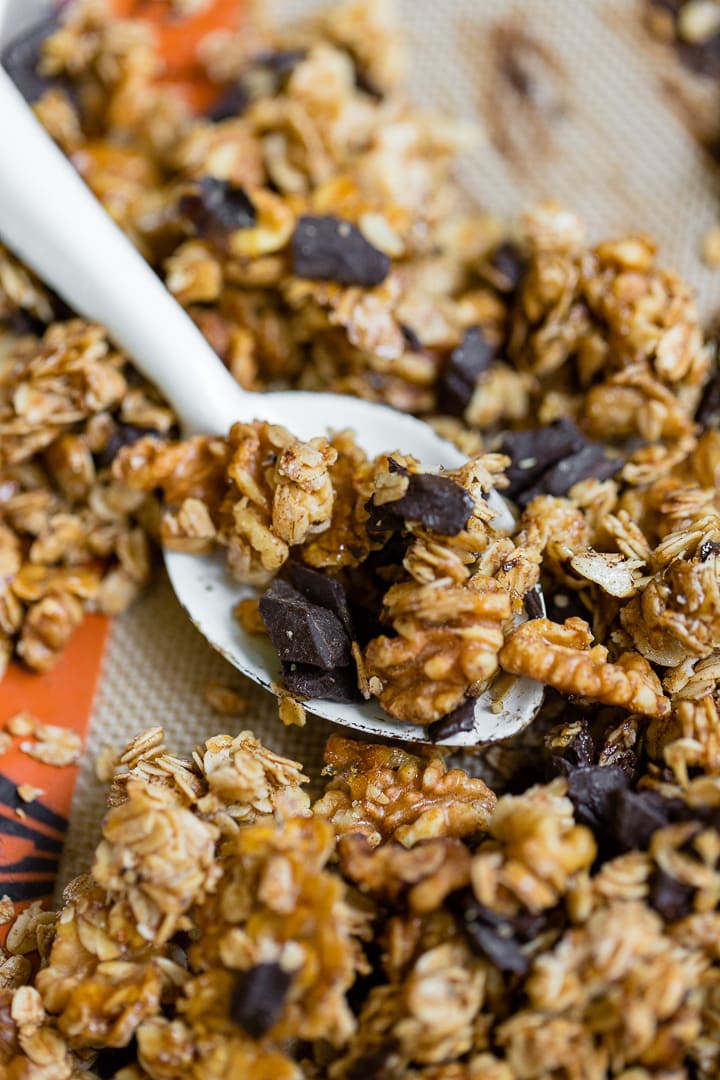 Close-up of a spoon stirring honey walnut granola just baked on a sheet pan.