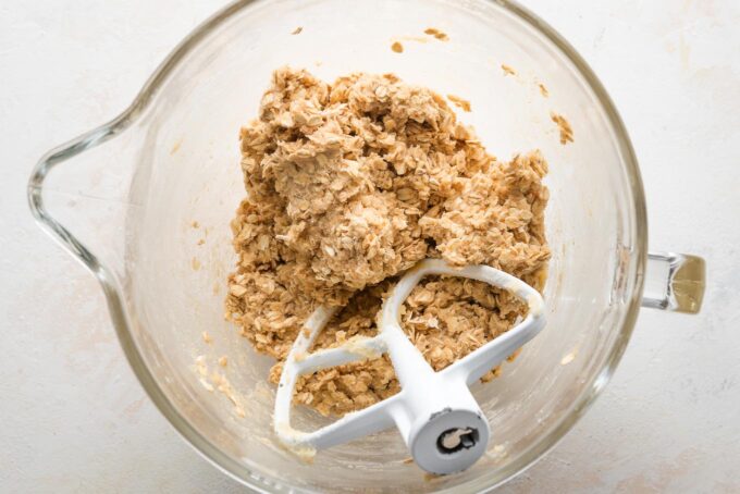 Oatmeal cookie dough mixed together in a clear stand mixer bowl.