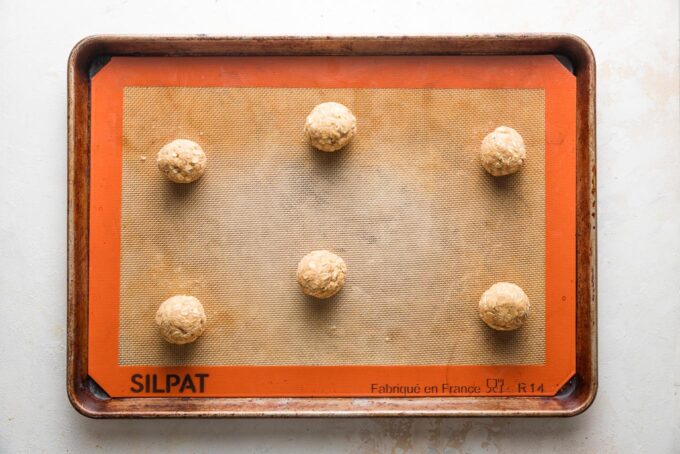 Balls of dough for oatmeal cookies, rolled into smooth balls and arranged several inches apart on a large baking sheet.
