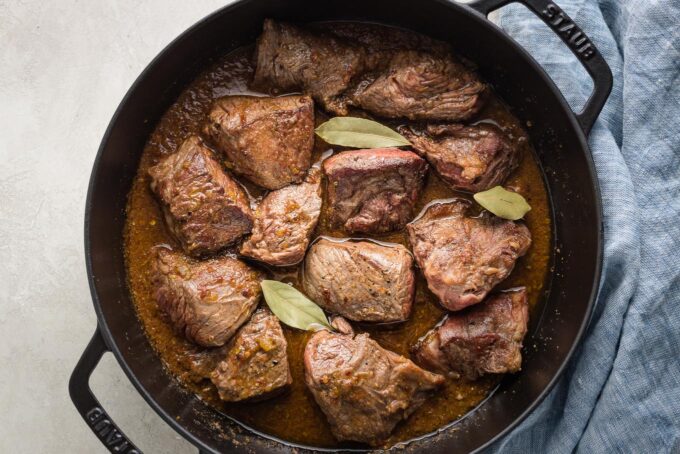 Pieces of seared chuck roast in a cast iron skillet.