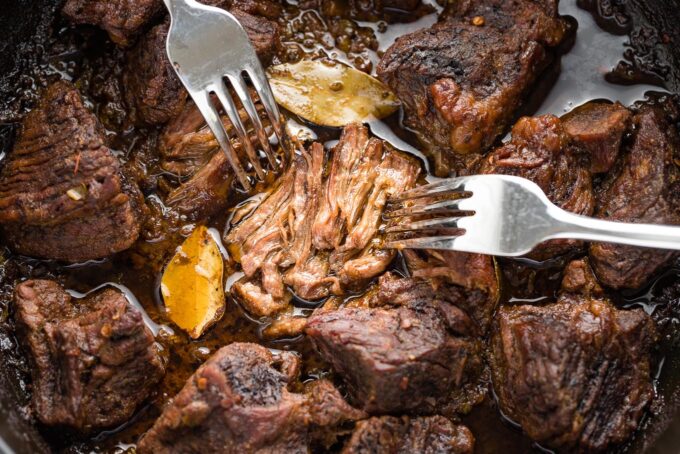 Close up of two forks shredding a piece of braised chuck roast.