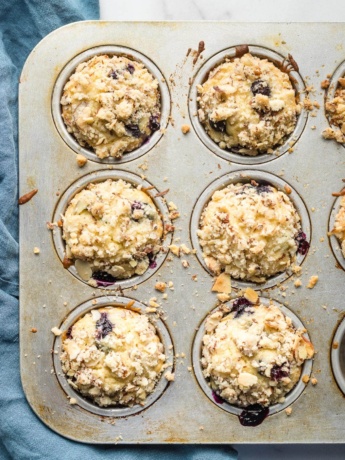 Six blueberry muffins with almond streusel topping in a baking tin.