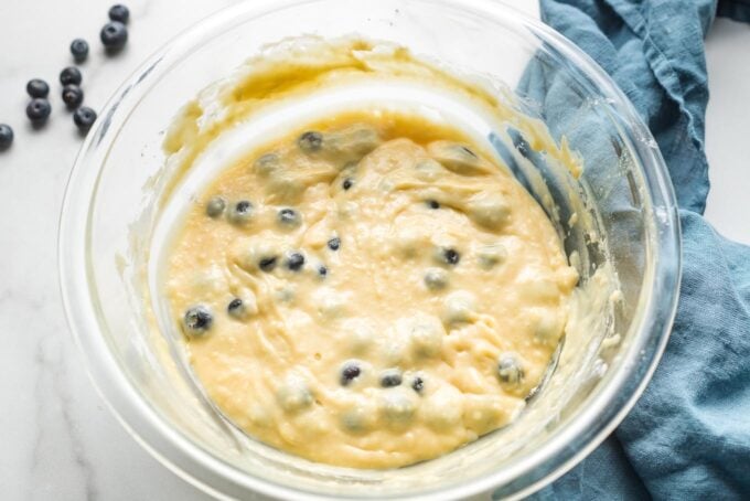 Clear glass prep bowl holding blueberry almond muffin batter.