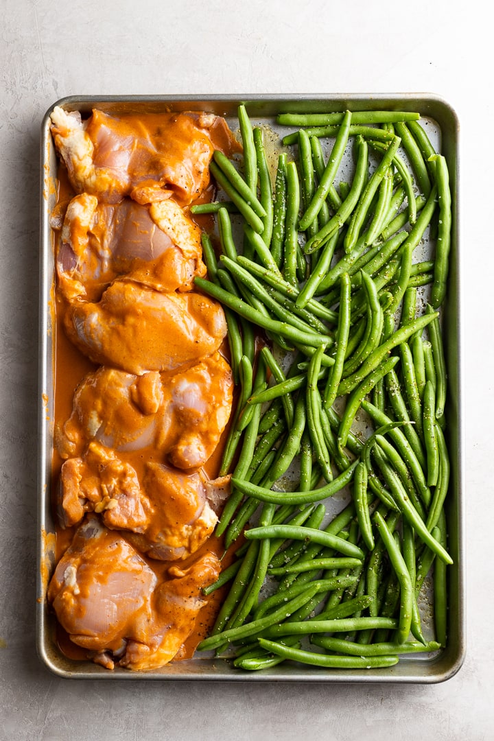 Chicken thighs in peanut sauce on baking sheet, ready to go into the oven.