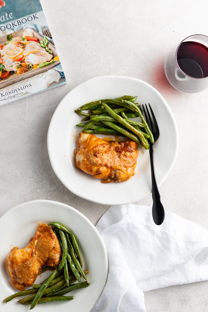 Plates of chicken thighs with peanut sauce and green beans, with a copy of The Ultimate One-Pan Oven Cookbook in the background.