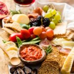 Photo of a gorgeous cheeseboard filled with cheese, crackers, meat, dip, veggies, and fruit.