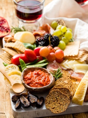 Photo of a gorgeous cheeseboard filled with cheese, crackers, meat, dip, veggies, and fruit.