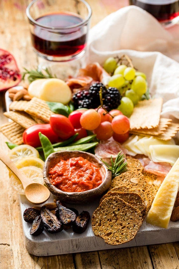 Photo of a gorgeous cheeseboard filled with cheese, crackers, meat, dip, veggies, and fruit.