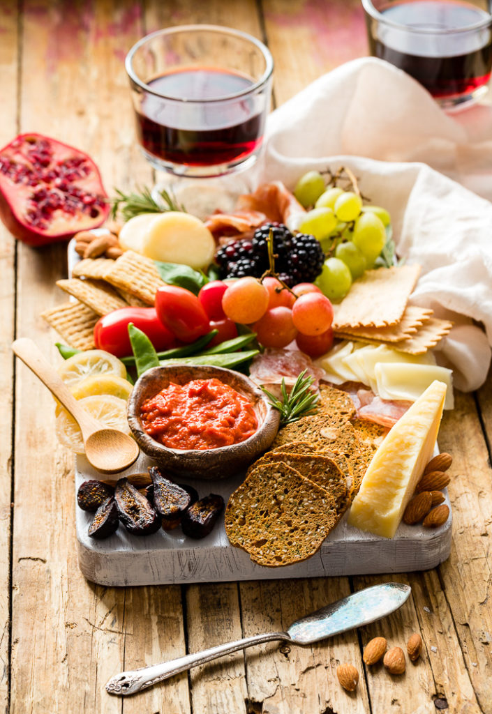 Photo of a gorgeous cheeseboard filled with cheese, crackers, meat, dip, veggies, and fruit.