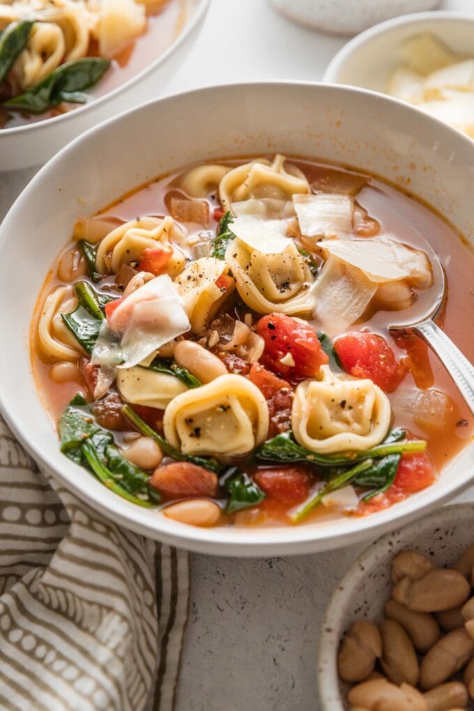 Angled view of white bean tortellini soup with tomatoes, spinach, and Italian herbs.