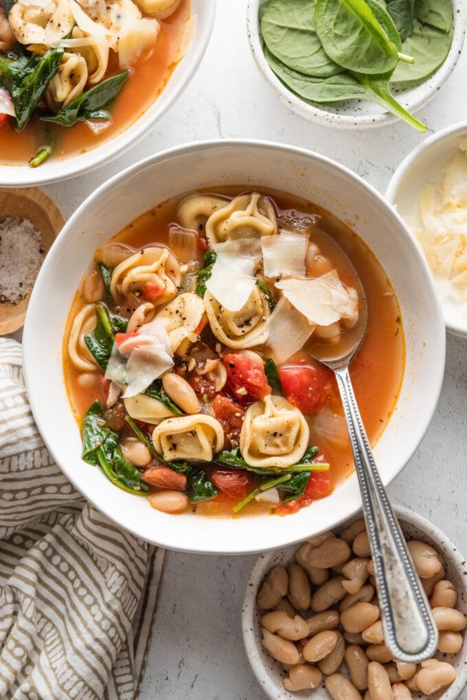 Bowl of white bean tortellini soup with baby spinach, fresh Parmesan, cracked salt and pepper.
