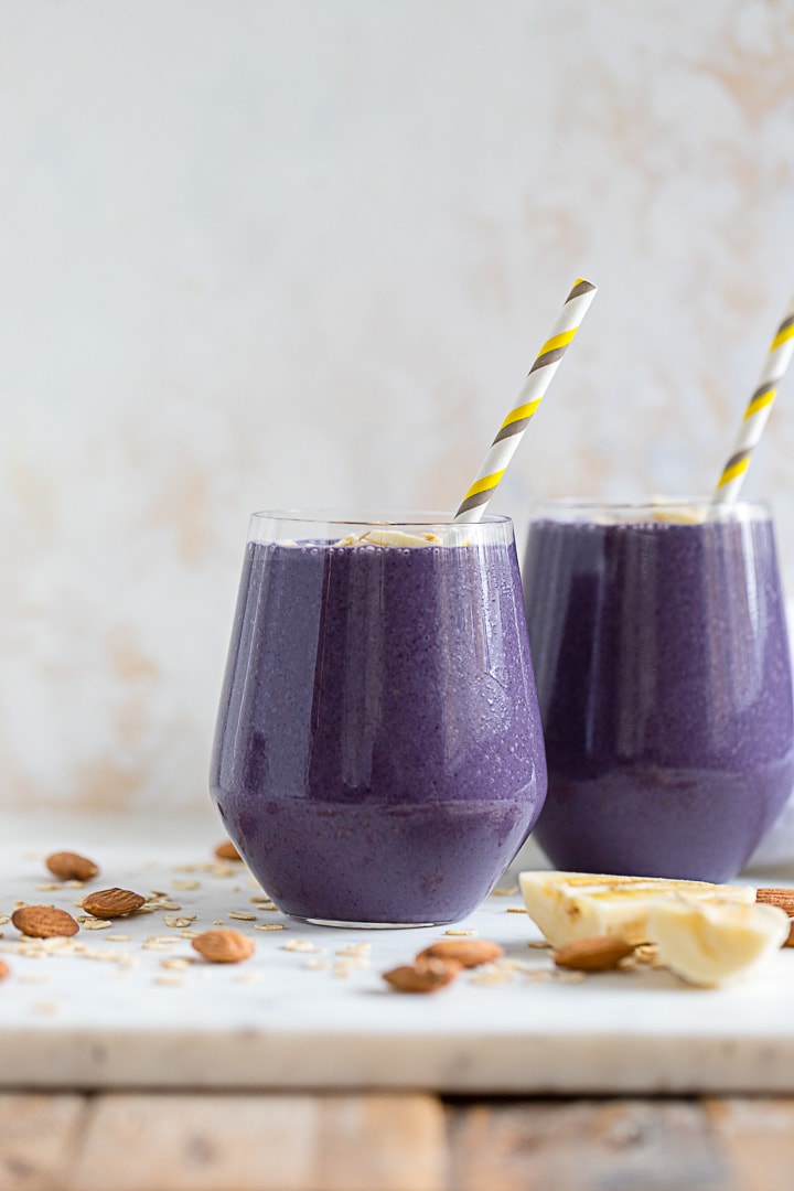 Two banana blueberry almond milk smoothies, ready to drink with paper straws.