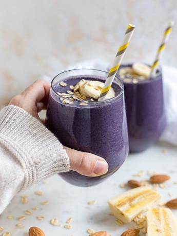 A hand holding a blueberry almond milk smoothie in a small glass with a straw.