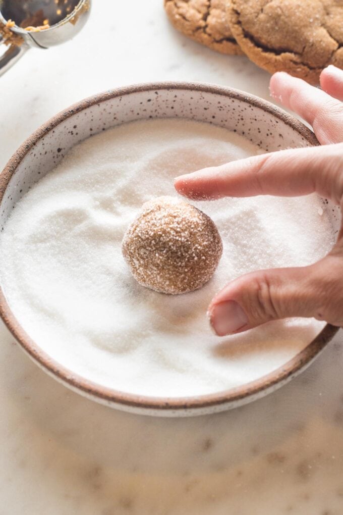 A ball of dough for a chewy ginger molasses cookie being rolled in extra white sugar before baking.