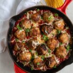 A large red Le Creuset cast iron pan filled with mozzarella-stuffed chicken Parmesan meatballs in marinara.