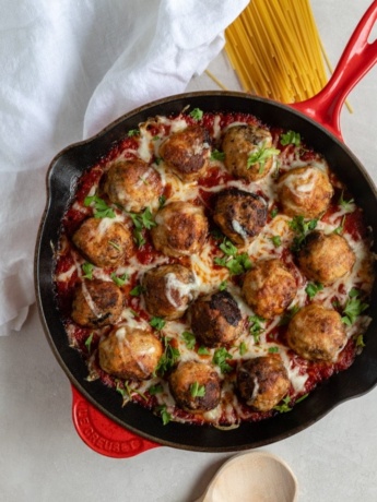 A large red Le Creuset cast iron pan filled with mozzarella-stuffed chicken Parmesan meatballs in marinara.