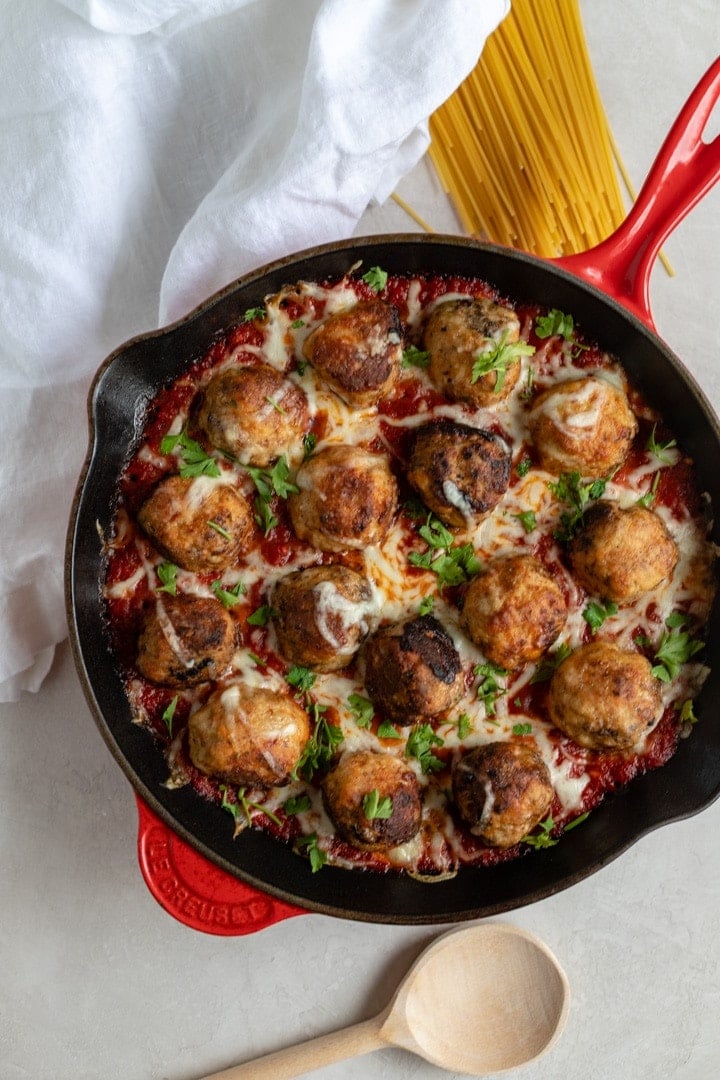 A large red Le Creuset cast iron pan filled with mozzarella-stuffed chicken Parmesan meatballs in marinara.