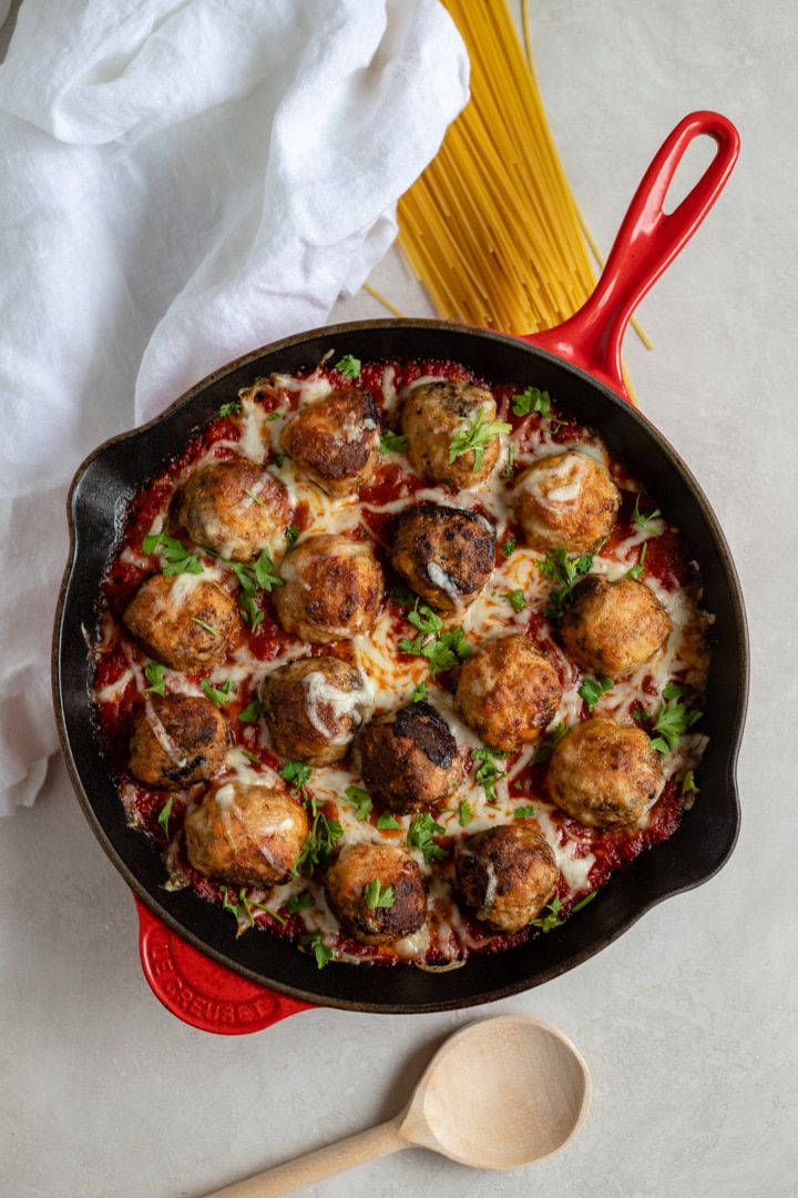 A large red Le Creuset cast iron pan filled with mozzarella-stuffed chicken Parmesan meatballs in marinara.