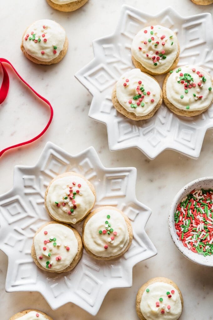 Snowflake plates holding batches of soft frosted eggnog sugar cookies with red and green sprinkles.
