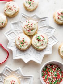 Snowflake plates holding batches of soft frosted eggnog sugar cookies with red and green sprinkles.