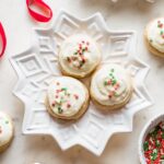 Snowflake plates holding batches of soft frosted eggnog sugar cookies with red and green sprinkles.