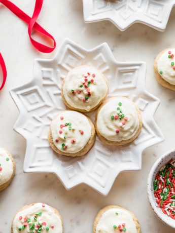 Snowflake plates holding batches of soft frosted eggnog sugar cookies with red and green sprinkles.