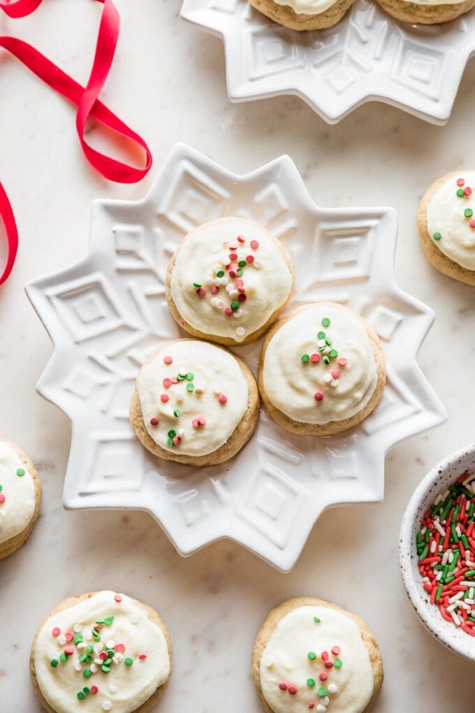 Snowflake plates holding batches of soft frosted eggnog sugar cookies with red and green sprinkles.