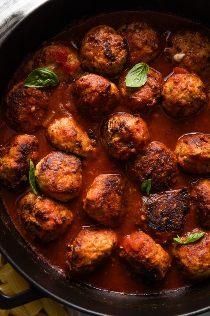 Chicken Parmesan meatballs in a deep skillet full of bubbling marinara sauce.