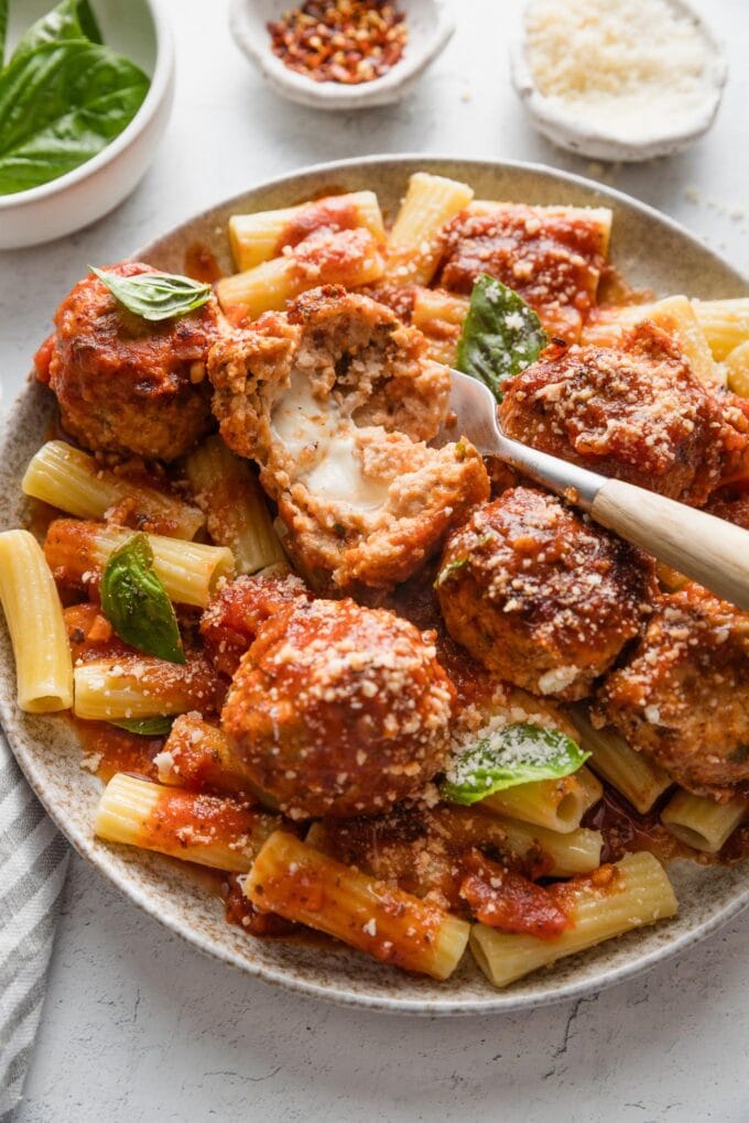 Plate with meatballs, rigatoni, marinara, Parmesan, and fresh basil.