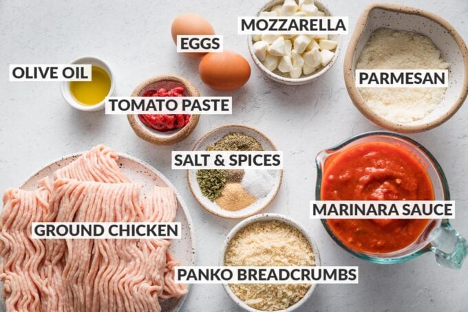 Labeled overhead photo of ground chicken, mozzarella pearls, grated Parmesan, two eggs, Panko breadcrumbs, marinara sauce, tomato paste, olive oil, salt, and spices.