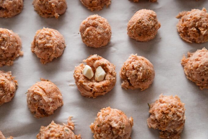 Uncooked chicken Parmesan meatballs with mozzarella pieces stuffed in the middle.