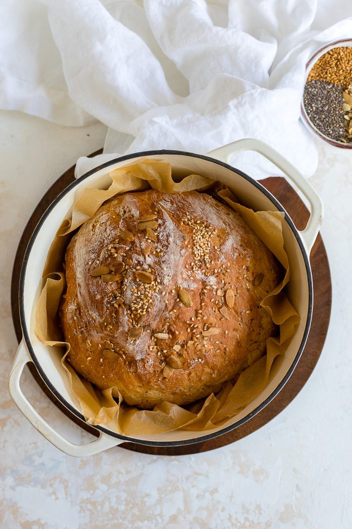 No knead bread with seeds baked in a white Dutch oven.