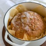 No knead bread with seeds baked in a white Dutch oven.