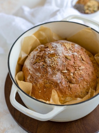 No knead bread with seeds baked in a white Dutch oven.