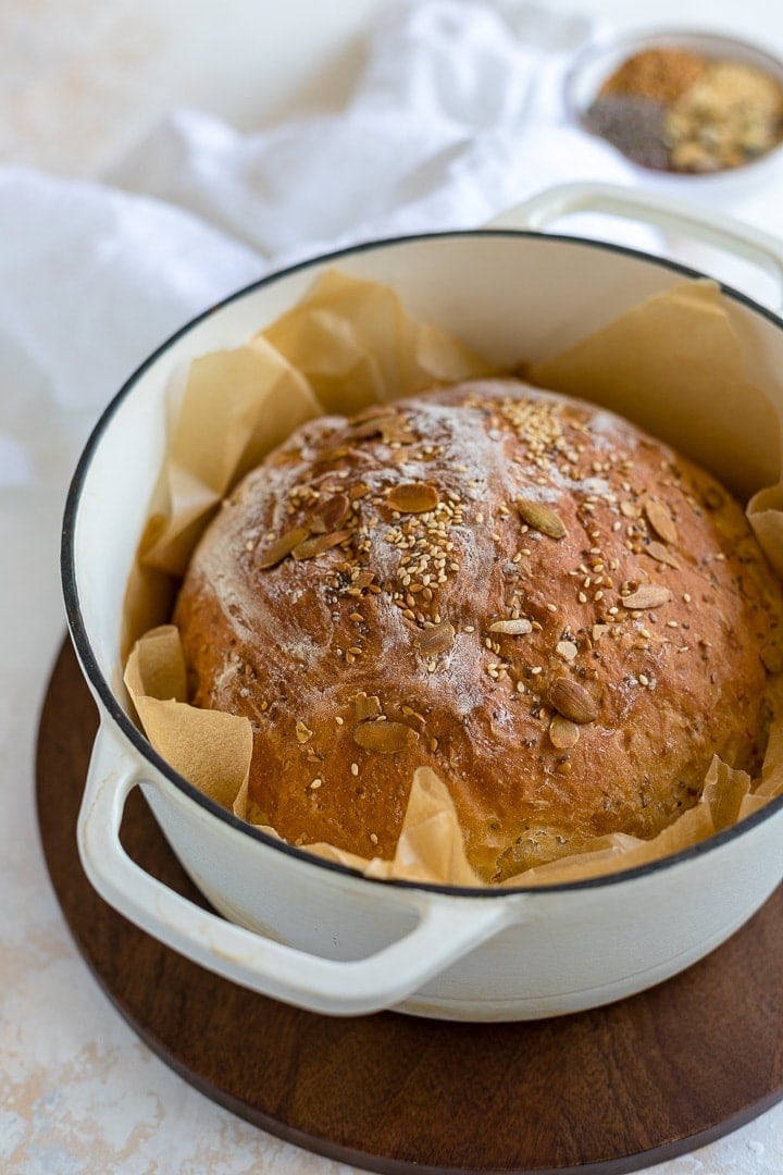 No knead bread with seeds baked in a white Dutch oven.