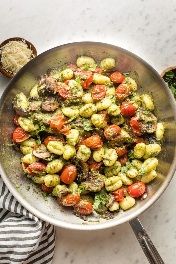 Skillet with gnocchi, pesto, mushrooms, and charred cherry tomatoes.