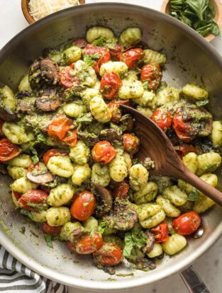 Skillet with gnocchi, pesto, mushrooms, and charred cherry tomatoes.
