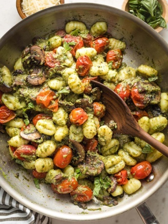 Skillet with gnocchi, pesto, mushrooms, and charred cherry tomatoes.