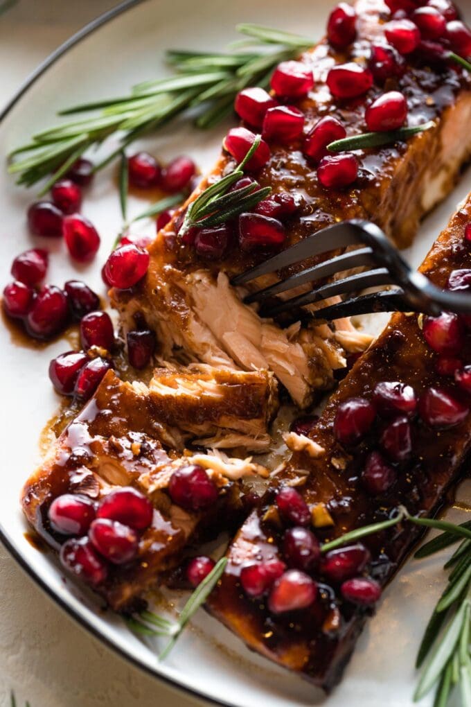 Close up image of a fork pulling apart flaky pieces of salmon glazed with pomegranate molasses.