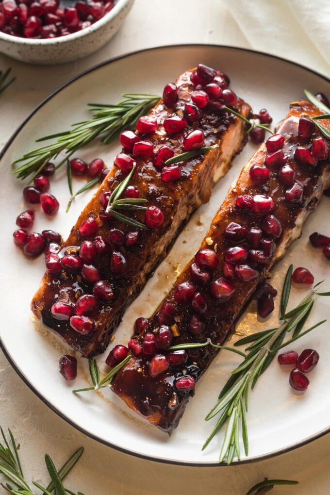 Plate with two filets of pomegranate salmon garnished with fresh rosemary.