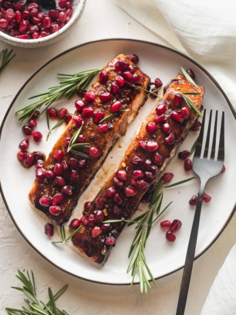 Plate with two filets of pomegranate salmon garnished with fresh rosemary.