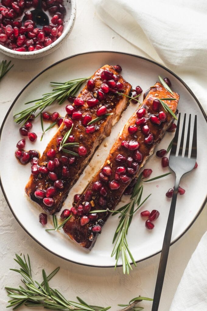 Plate with two filets of pomegranate salmon garnished with fresh rosemary.