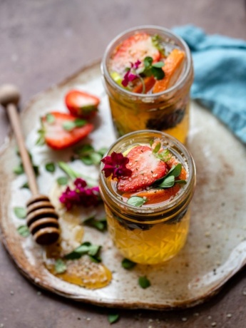 Two tequila kombucha cocktails with fresh herbs and fruit arranged on a small platter with a drizzle of honey.