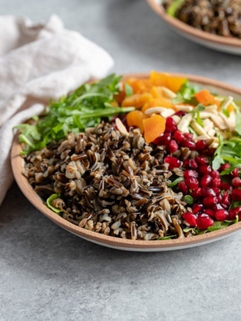 A bowl of wild rice winter salad with arugula, pomegranate arils, almonds, and dried apricots.